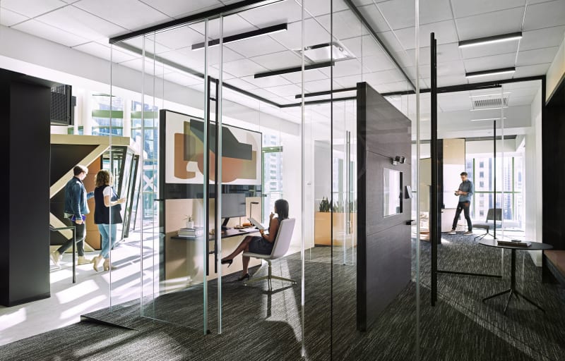 These office spaces are surrounded by DIRTT's Reflect glass wall system with top-mounted sliding glass barn doors.