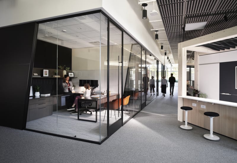 Private offices made from Reflect glass walls and angled solid DIRTT walls line one side of a hallway.