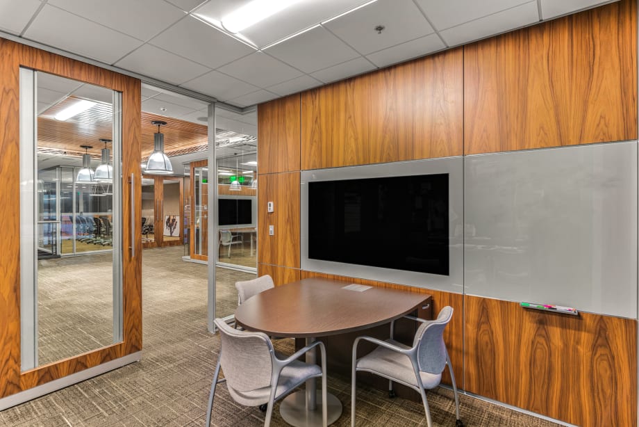 A private meeting room with sliding glass door and solid veneer modular walls with integrated tech and writeable surfaces.