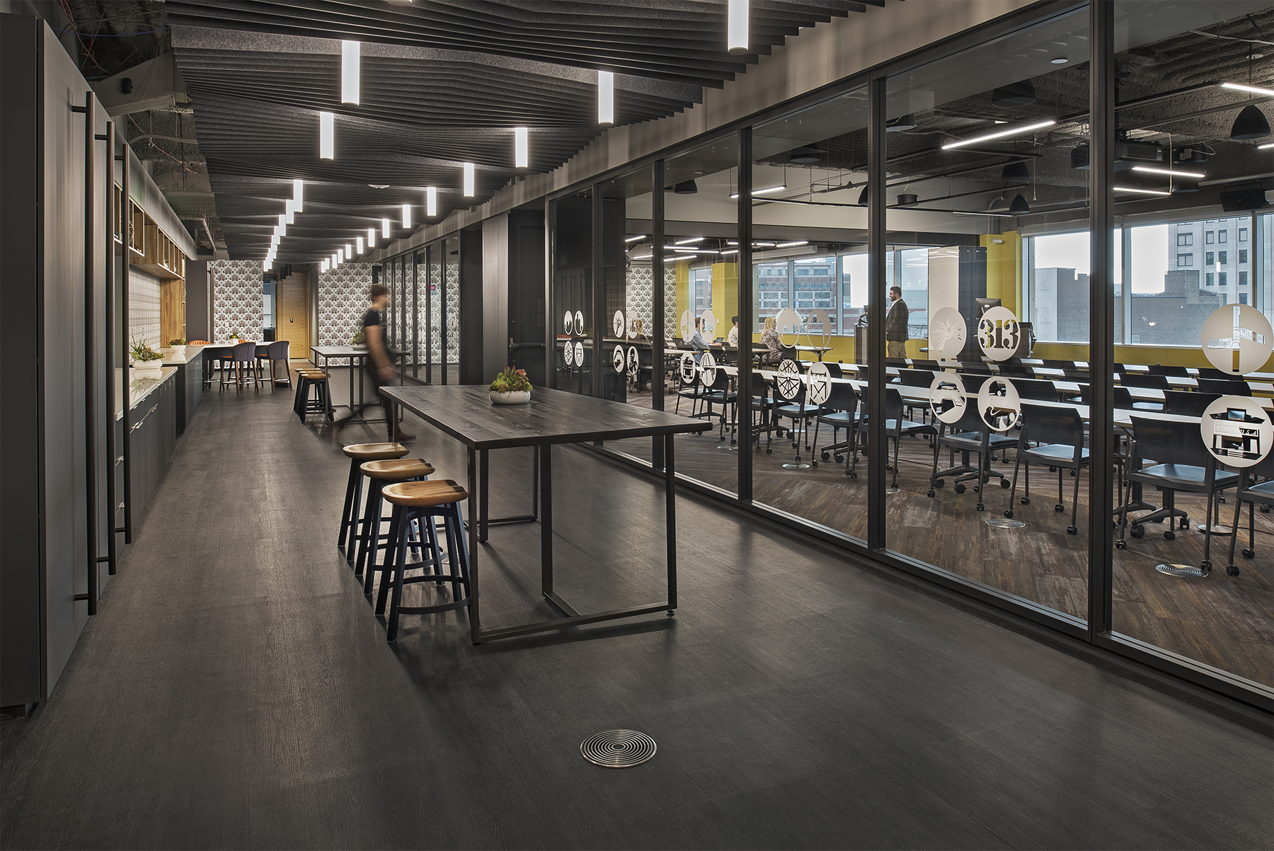 A modular glass wall system separates a classroom from a modern kitchen area that features custom casework.