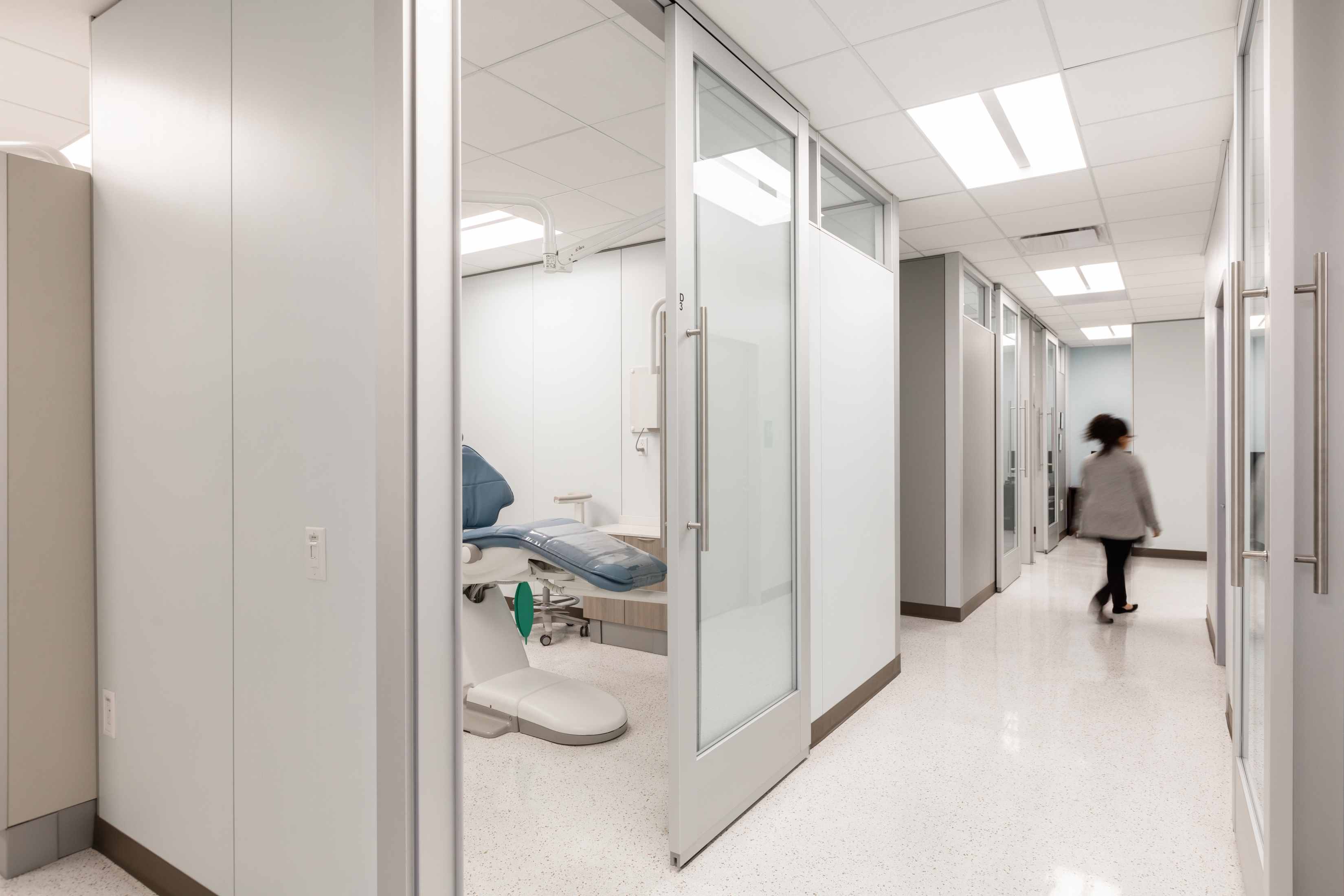 From the hallway we see a private dental treatment area made from DIRTT's glass and solid walls with sliding glass door.