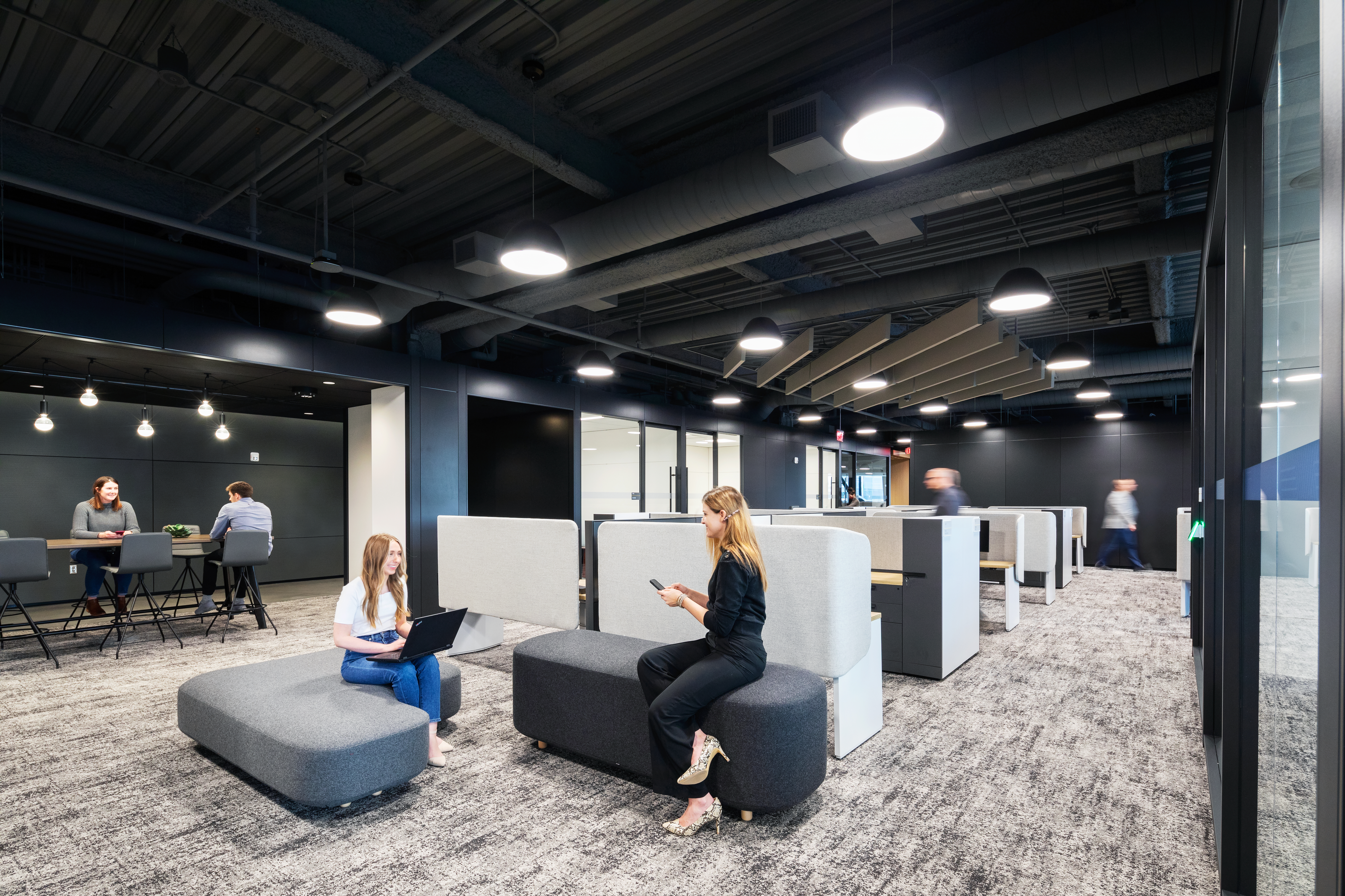 Casual lounge seating in the middle of an open space is flanked by modular glass wall enclosed offices and an open meeting room.