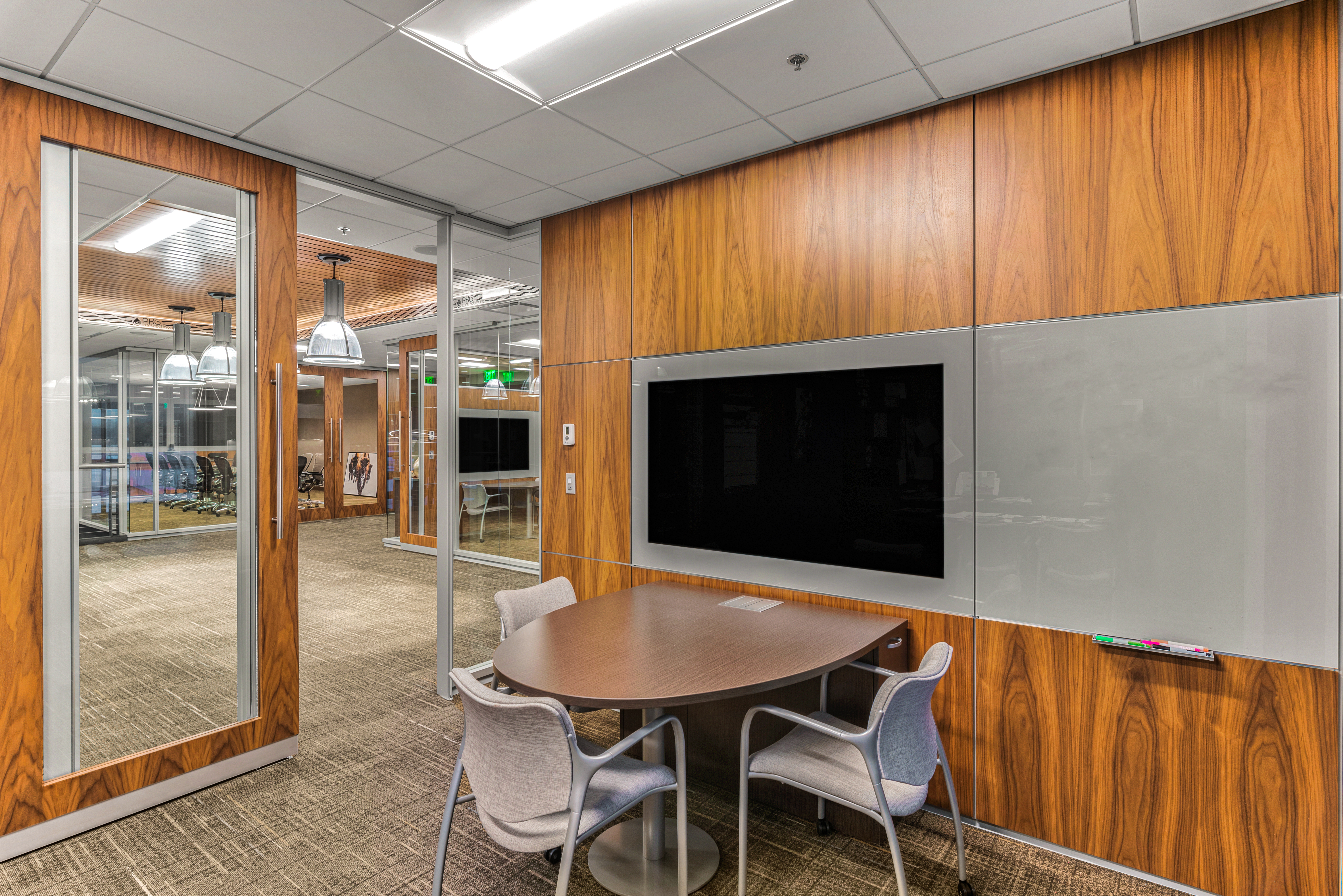 A private meeting room with sliding glass door and solid veneer modular walls with integrated tech and writeable surfaces.